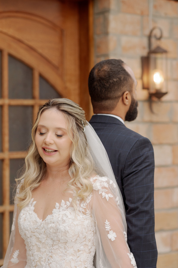 Noiva Claudia de olhos fechados em momento de oração durante o first touch em Jacareí. O noivo Matheus está posicionado de costas, mantendo a conexão antes do altar. Fotografia de casamento emocionante capturada por Gilson Dias.