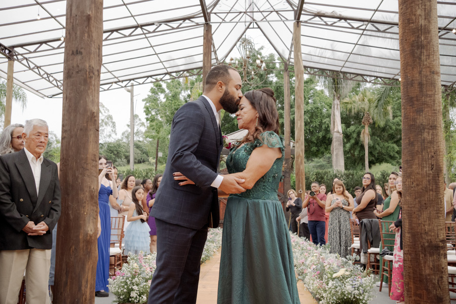 Noivo Matheus beija a testa de sua mãe no altar em cerimônia ao ar livre no Boulevard Jacareí. Momento de carinho e gratidão capturado pela fotografia de casamento de Gilson Dias, destacando as conexões reais da família.
