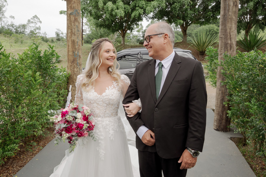 Noiva Claudia sorri para seu pai antes da entrada na cerimônia ao ar livre em Jacareí. Fotografia de casamento no Boulevard capturando a cumplicidade e o carinho entre pai e filha pelo fotógrafo Gilson Dias.