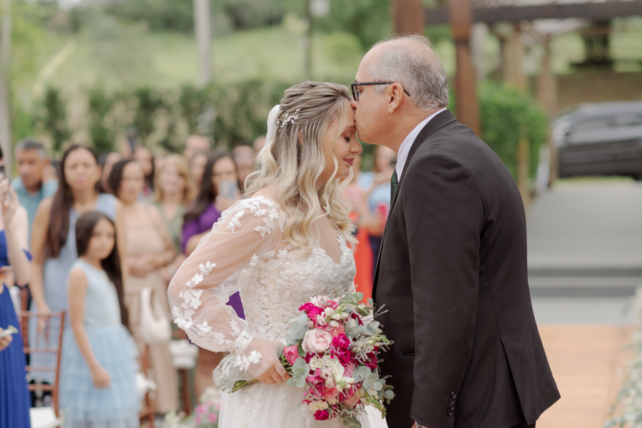 Pai da noiva Claudia beija sua testa em momento de despedida no altar da cerimônia ao ar livre no Boulevard Jacareí. Fotografia de casamento emocionante capturando o amor familiar e a tradição, registrada pelo fotógrafo Gilson Dias.
