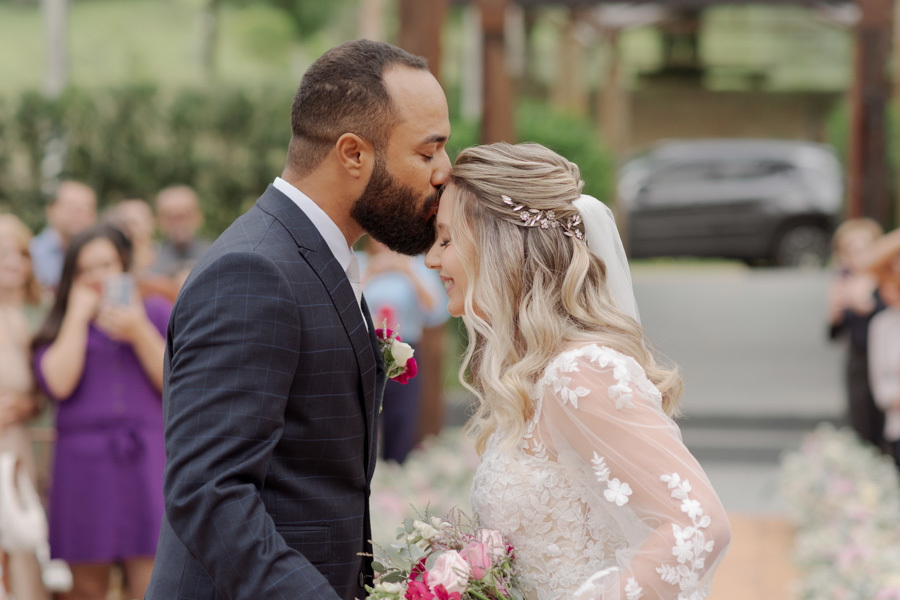 Noivo Matheus beija a testa da noiva Claudia no altar durante cerimônia ao ar livre no Boulevard Jacareí. Fotografia de casamento emocionante capturando o carinho e a união do casal, registrada pelo fotógrafo Gilson Dias.