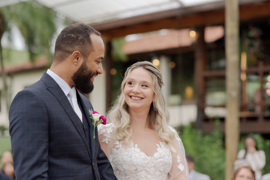 Noiva Claudia e noivo Matheus trocam olhares apaixonados e sorrisos no altar durante cerimônia ao ar livre no Boulevard Jacareí. Fotografia de casamento capturando a felicidade e o amor do casal, registrada pelo fotógrafo Gilson Dias.