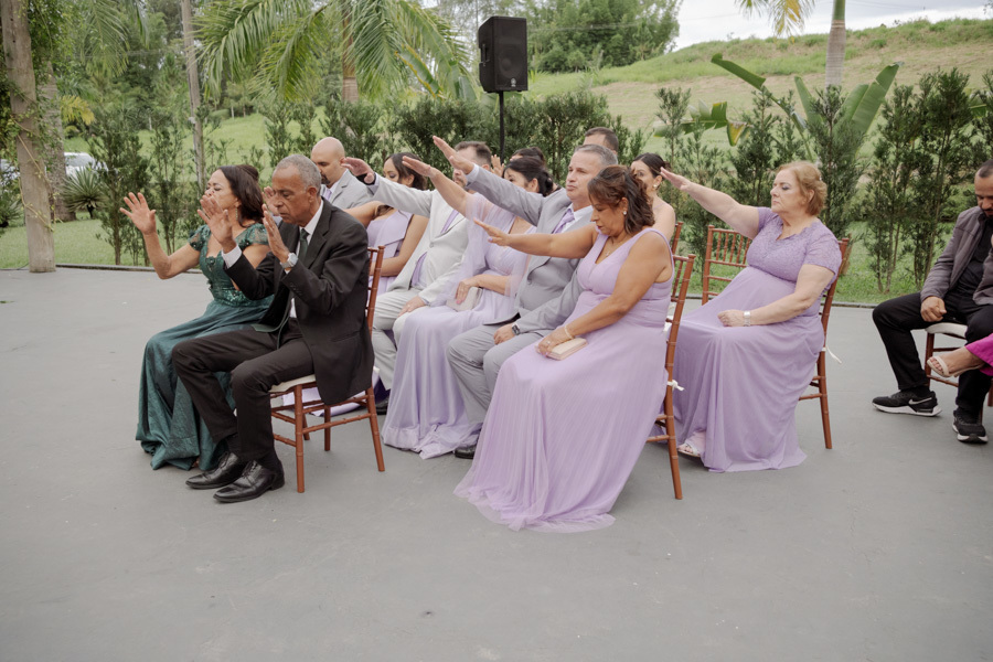 Padrinhos e familiares estendem as mãos em benção durante a cerimônia de Claudia e Matheus no Boulevard Jacareí. Fotografia de casamento que registra a espiritualidade e o apoio da família ao ar livre, capturada pelo fotógrafo Gilson Dias.