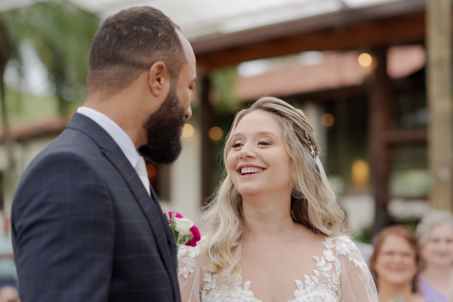 Noiva Claudia sorri com felicidade extrema para o noivo Matheus no altar do Boulevard Jacareí. Fotografia de casamento em close capturando a alegria contagiante e o amor genuíno do casal durante a cerimônia, registrada por Gilson Dias.