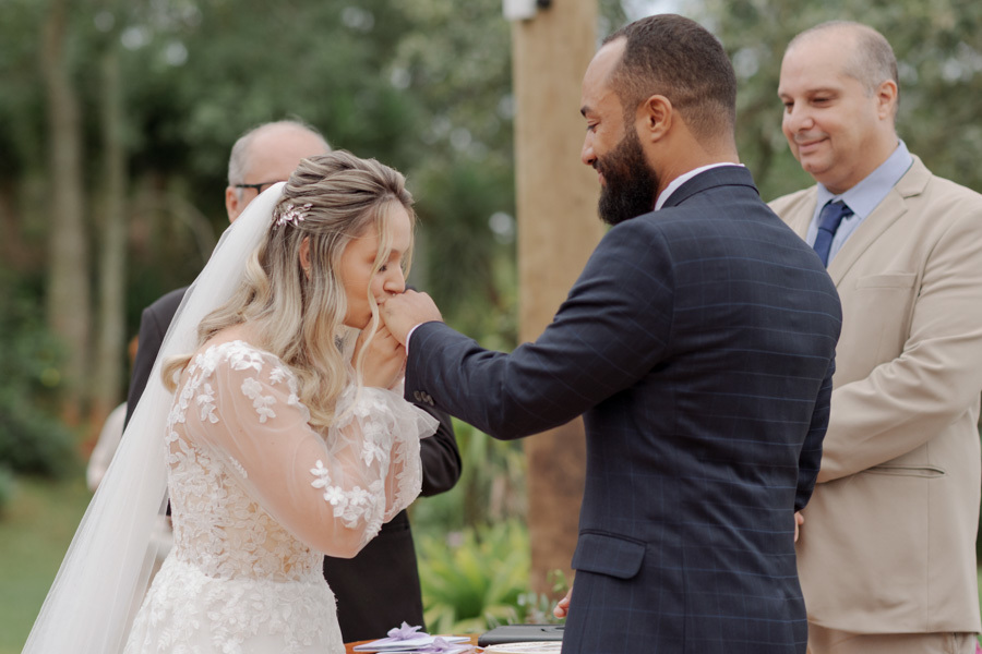 Noiva Claudia beija a mão do noivo Matheus após a troca de votos no altar do Boulevard Jacareí. O momento de carinho e gratidão durante a cerimônia ao ar livre é registrado com sensibilidade pelo fotógrafo de casamento Gilson Dias.