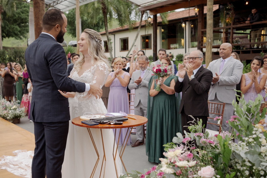 Noiva Claudia e noivo Matheus sorriem após o primeiro beijo no altar do Boulevard Jacareí. Padrinhos e familiares aplaudem ao fundo em um momento de celebração e alegria na cerimônia ao ar livre, registrada pelo fotógrafo Gilson Dias.