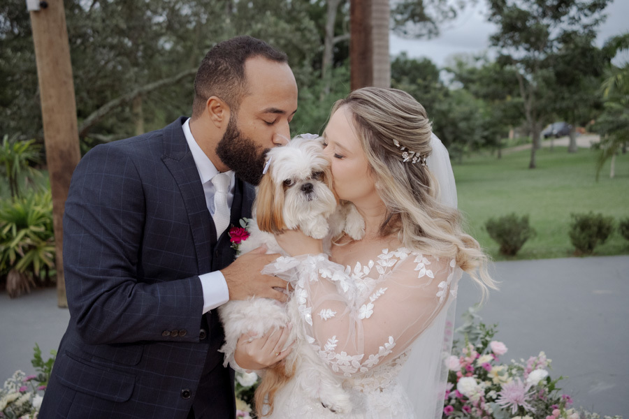 Noivos Claudia e Matheus beijam seu cachorro de estimação no altar do Boulevard Jacareí. Fotografia de casamento carinhosa incluindo o pet na celebração ao ar livre, registrada com sensibilidade pelo fotógrafo Gilson Dias.