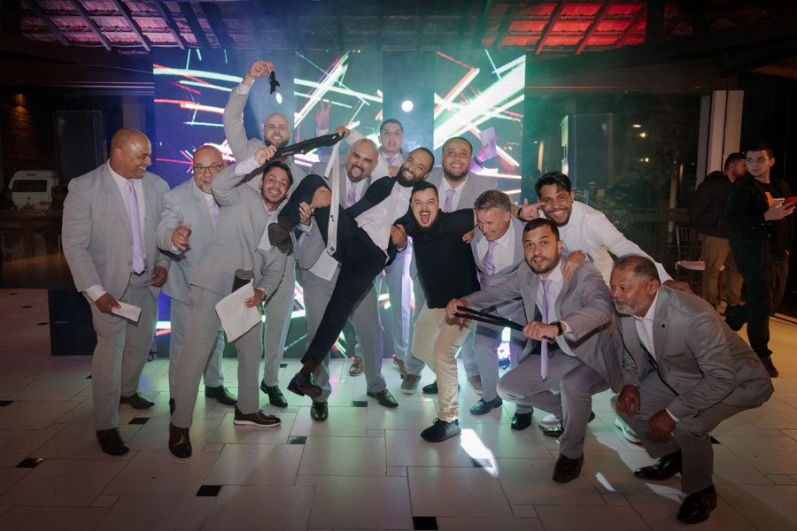Noivo Matheus é carregado e celebrado pelos padrinhos na pista de dança do Boulevard Jacareí. Fotografia de casamento animada capturando a diversão dos convidados e a energia da festa, registrada com alegria pelo fotógrafo Gilson Dias.