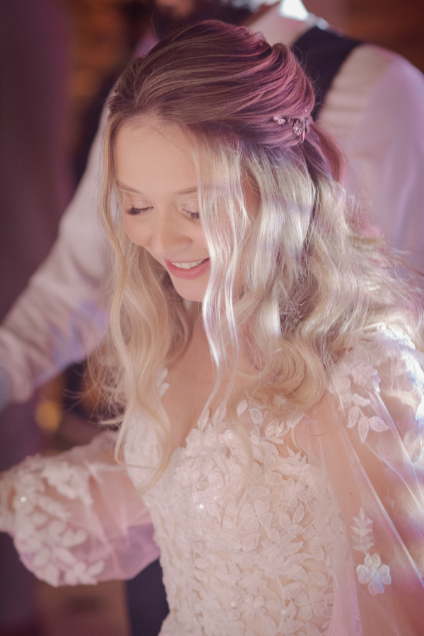 Close da noiva Claudia sorrindo e olhando para baixo durante a festa no Boulevard Jacareí. A iluminação suave destaca os detalhes do vestido rendado e o penteado semipreso, em registro delicado feito pelo fotógrafo Gilson Dias.