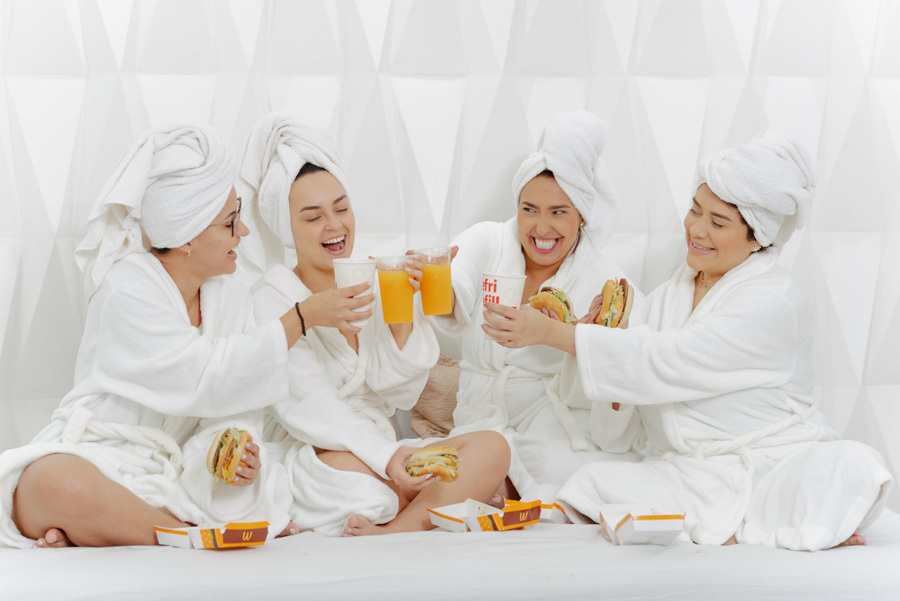 Noiva e madrinhas brindam com lanches e sorrisos durante o making of em Taubaté. Cena descontraída no Espaço Verde Vale, capturando a amizade e alegria antes da cerimônia com fotografia espontânea e natural no Vale do Paraíba.