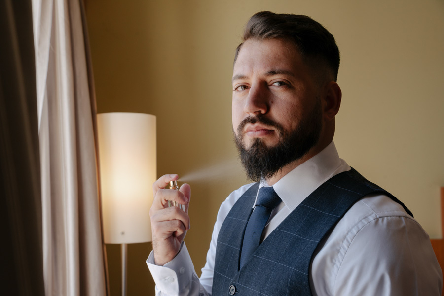 Noivo borrifa perfume durante o making of em São José dos Campos. Retrato masculino elegante com foco nos preparativos finais, capturado pelo fotógrafo Gilson Dias para o casamento com a Thayná no Vale do Paraíba.