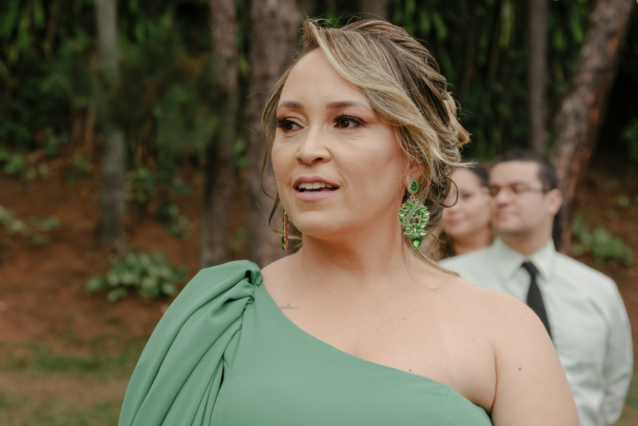 Madrinha de casamento em vestido verde observa emocionada a cerimônia ao ar livre no Espaço Verde Vale, Taubaté. Fotografia de casamento no Vale do Paraíba focada em expressões e sentimentos reais, capturada pelo fotógrafo Gilson Dias.