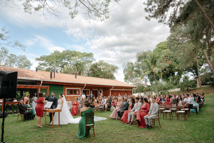 Visão panorâmica da cerimônia de casamento ao ar livre no Espaço Verde Vale, em Taubaté. Noivos Thayná e Diego no altar sob céu nublado, cercados por convidados em um cenário natural e emocionante registrado por Gilson Dias Fotografia no Vale do Paraíba.