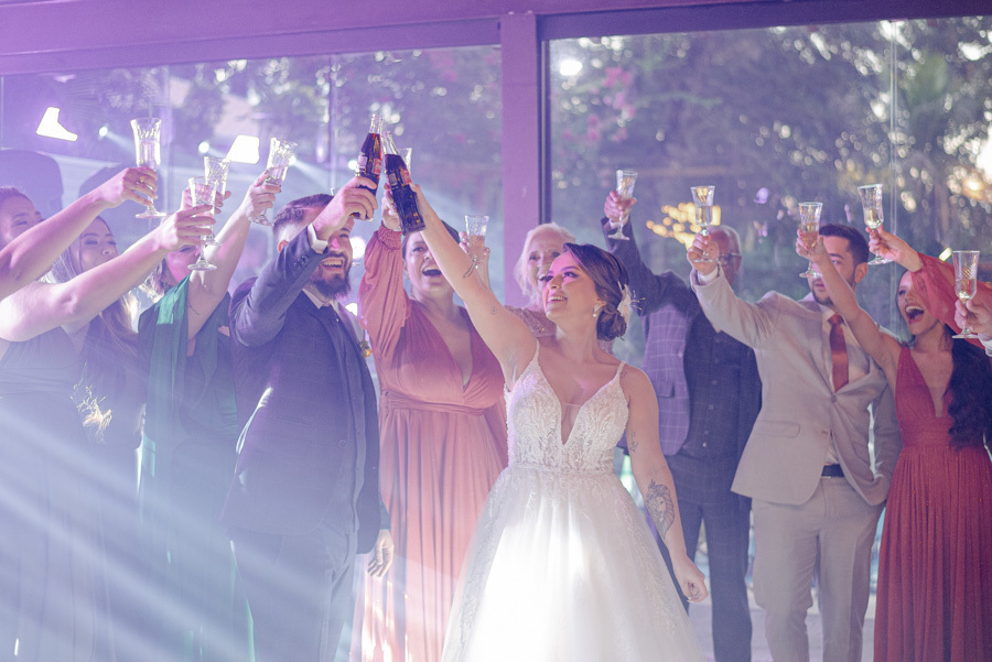 Noivos Thayná e Diego brindam com padrinhos durante a festa no Espaço Verde Vale, Taubaté. Fotografia de casamento animada com luzes de balada, capturando o brinde coletivo e a alegria da recepção no Vale do Paraíba por Gilson Dias Fotografia.