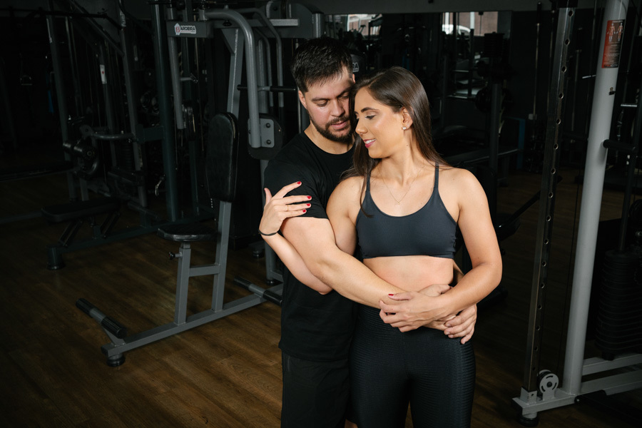 Close do casal Matthaus e Rebeca abraçados e sorridentes durante ensaio pré-wedding na Academia Aroeira. Foto espontânea capturada por fotógrafo profissional em Jacareí, destacando a cumplicidade e o carinho em um cenário fitness autêntico.