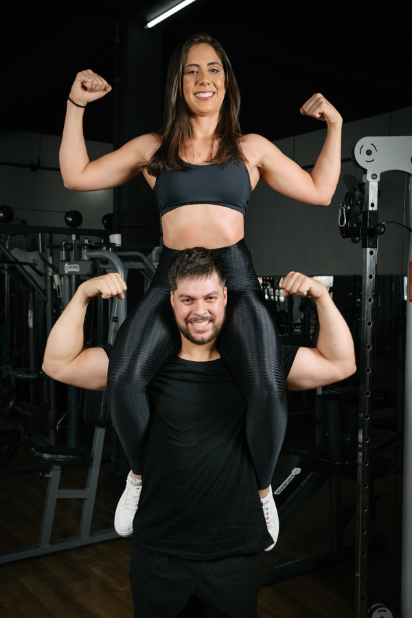 Matthaus e Rebeca celebram o ensaio pré-wedding na Academia Aroeira com pose descontraída de força. Registro de fotógrafo profissional em Jacareí que une amor, saúde e diversão em imagens espontâneas com identidade única do casal.