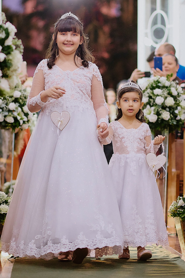 As duas filhas de Paloma e Cassiano entram como daminhas na Capela Nossa Senhora Aparecida, em São José dos Campos. Vestidas de branco com tiaras, elas carregam corações de pérolas, simbolizando a união da família durante a cerimônia de casamento.Noivo Ca