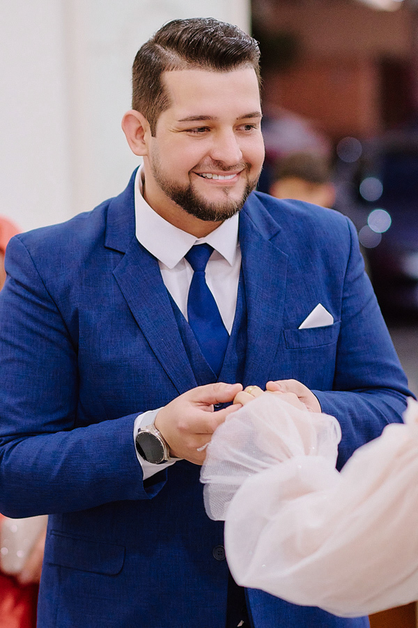 Noivo Cassiano sorri ao colocar a aliança no dedo de Paloma na Capela Nossa Senhora Aparecida, em São José dos Campos. Fotografia documental focada na emoção e no compromisso do casal durante a troca de alianças no altar.