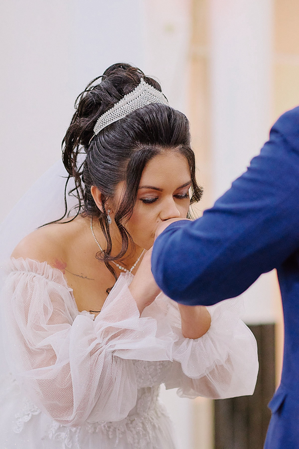 Noiva Paloma beija a mão de Cassiano após a troca de alianças na Capela Nossa Senhora Aparecida, São José dos Campos. Fotografia documental de casamento capturando um gesto de carinho e devoção no altar durante a cerimônia religiosa.