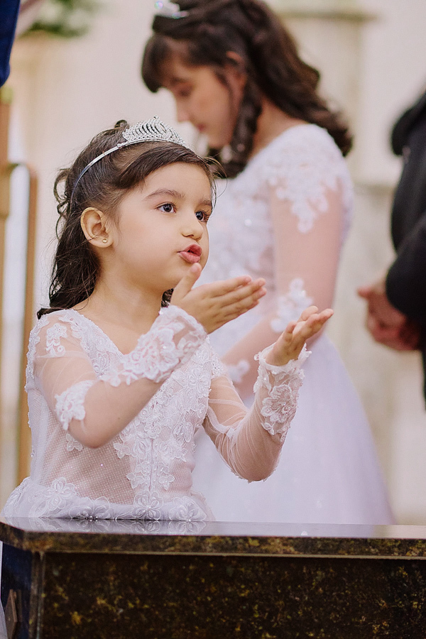 Daminha de casamento em São José dos Campos manda um beijo carinhoso durante a cerimônia na Capela Nossa Senhora Aparecida. Fotografia documental capturando a pureza e a participação das filhas no casamento de Paloma e Cassiano.