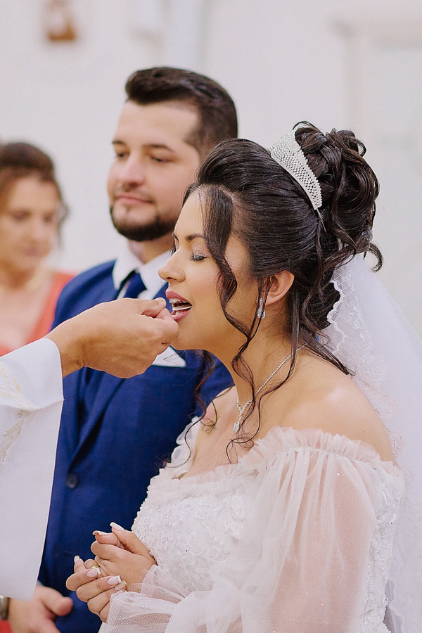 Noiva Paloma recebe a comunhão durante a celebração religiosa na Capela Nossa Senhora Aparecida, em São José dos Campos. Fotografia documental de casamento capturando a fé e a espiritualidade do casal Cassiano e Paloma no altar.