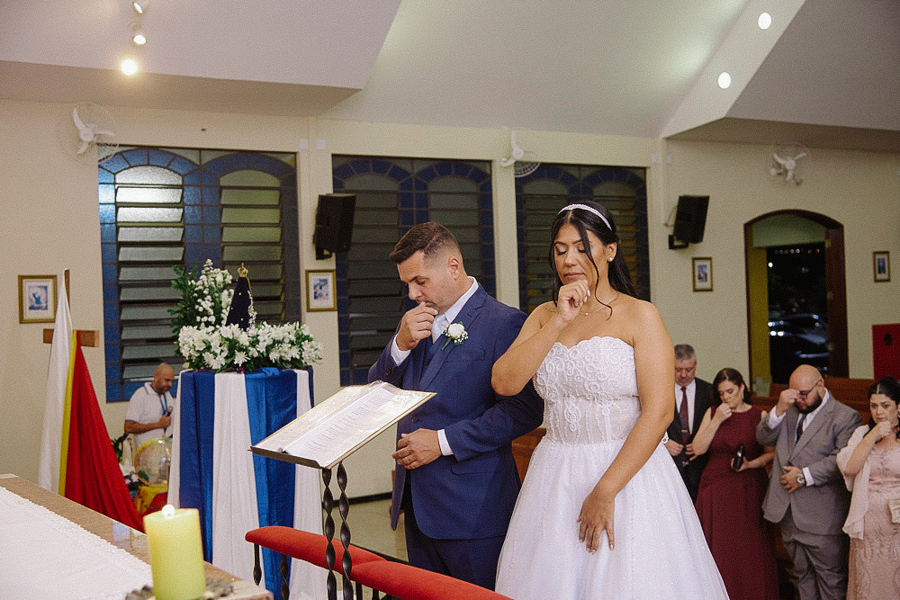 Noivos Marcela e Fernando emocionados no altar da Igreja Santa Maria em Jacareí. O casal enxuga as lágrimas durante a cerimônia religiosa, acompanhados por padrinhos também comovidos ao fundo. Fotografia de casamento sensível.