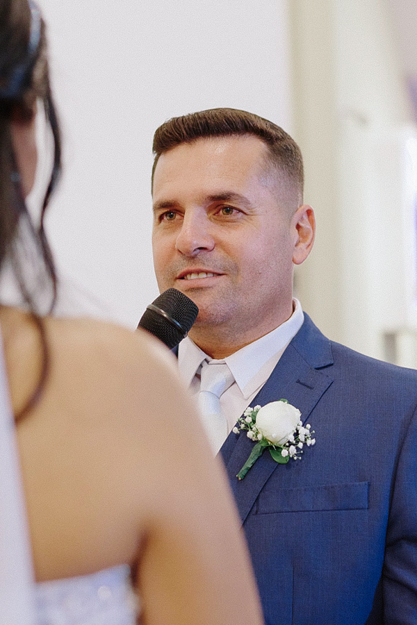 Close do noivo Fernando declarando seus votos emocionado para a noiva Marcela. Ele segura o microfone e olha nos olhos dela durante a cerimônia na Igreja Santa Maria. Fotografia de casamento em Jacareí capturando a sinceridade do momento.