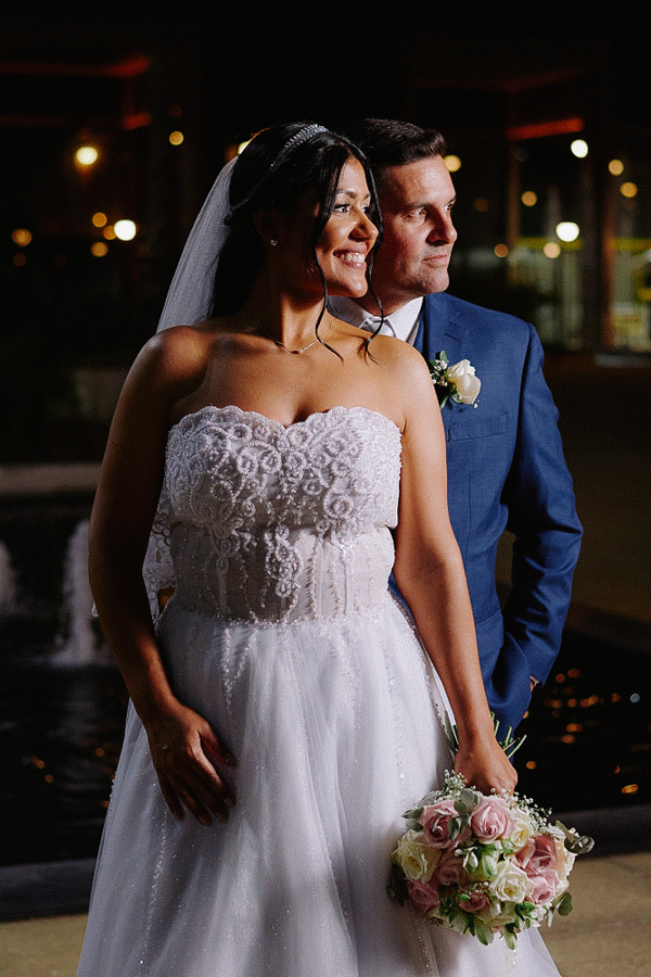 Retrato elegante do noivo Fernando sorrindo para a câmera durante ensaio de casamento noturno em Jacareí. Ele veste terno azul clássico.