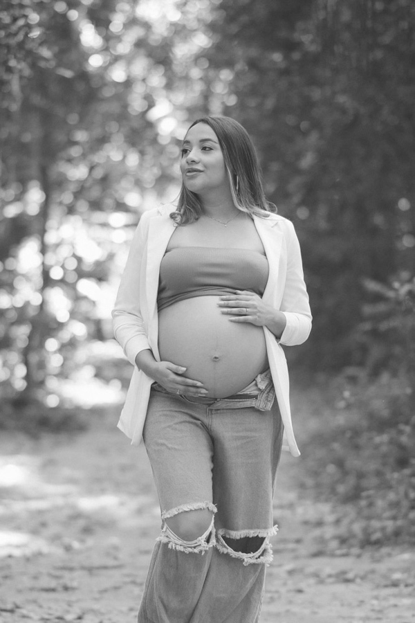 Foto de gestante em preto e branco em São José dos Campos. Lorrana caminha pelo Parque da Cidade com as mãos na barriga à espera de Pedro. A imagem destaca o contraste e a elegância da fotografia de maternidade com foco na expressão e na natureza.