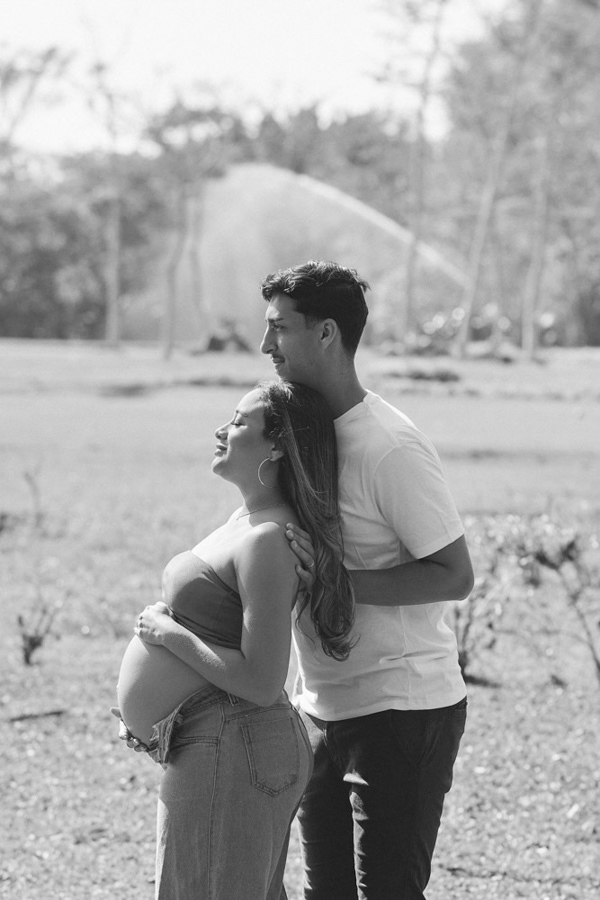 Fotógrafo de gestante em São José dos Campos. Lorrana e Felipe posam de perfil em P&B no Parque da Cidade. Ela exibe a barriga à espera de Pedro enquanto ele repousa o rosto em seu ombro, criando uma memória eterna de conexão e leveza na natureza.