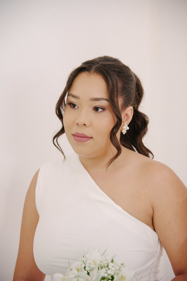 Retrato da noiva Gabrielle durante seu casamento civil em SJC. Ela usa um vestido branco de um ombro só, brincos de pérola e segura um buquê de flores brancas. Fotografia de casamento civil em São José dos Campos focada na delicadeza e emoção da noiva.