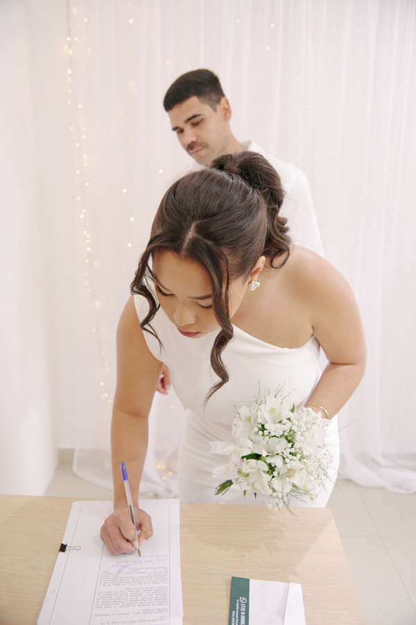 Fotografia de casamento civil em SJC: noiva Gabrielle assina a ata de casamento enquanto segura seu buquê. O registro foca na importância desse gesto solene em São José dos Campos, capturando o início oficial de uma nova história de amor.