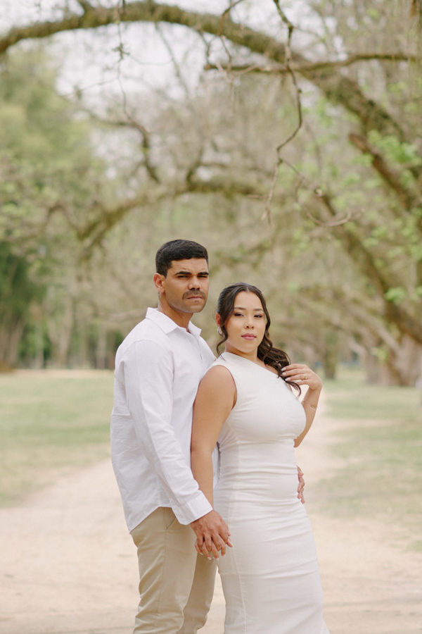 Fotografia de casamento em SJC: Gabrielle e Luiz Carlos posam de mãos dadas em um caminho arborizado no Parque da Cidade. O registro destaca a elegância e a união do casal durante o ensaio pós-civil em São José dos Campos.