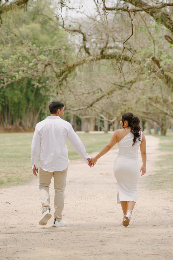 Ensaio de casamento em SJC: Gabrielle e Luiz Carlos caminham de mãos dadas por uma trilha arborizada no Parque da Cidade. O registro de costas simboliza o início da nova jornada do casal após o casamento civil em São José dos Campos.