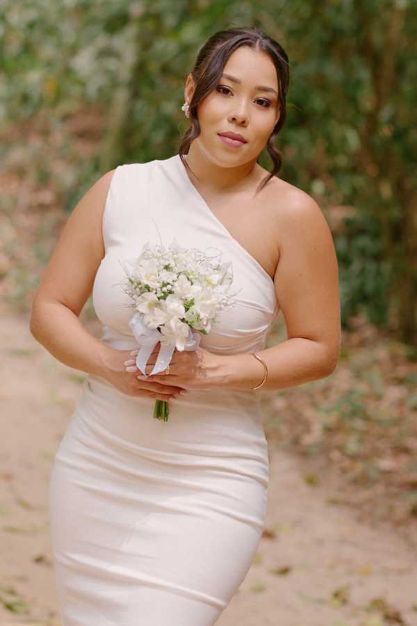 Fotografia de casamento em SJC: Retrato de corpo inteiro da noiva Gabrielle no Parque da Cidade. Ela usa um vestido branco elegante e segura seu buquê, destacando a beleza e a serenidade do ensaio pós-civil em São José dos Campos.