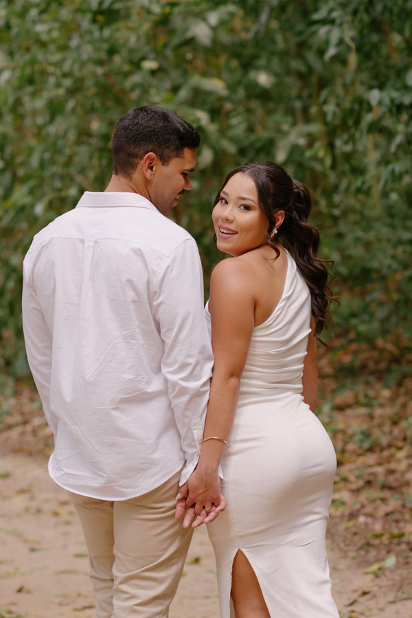 Fotografia de casamento em SJC: Gabrielle olha para trás com um sorriso radiante enquanto caminha de mãos dadas com Luiz Carlos. O registro captura a felicidade espontânea da noiva durante o ensaio pós-civil em São José dos Campos.