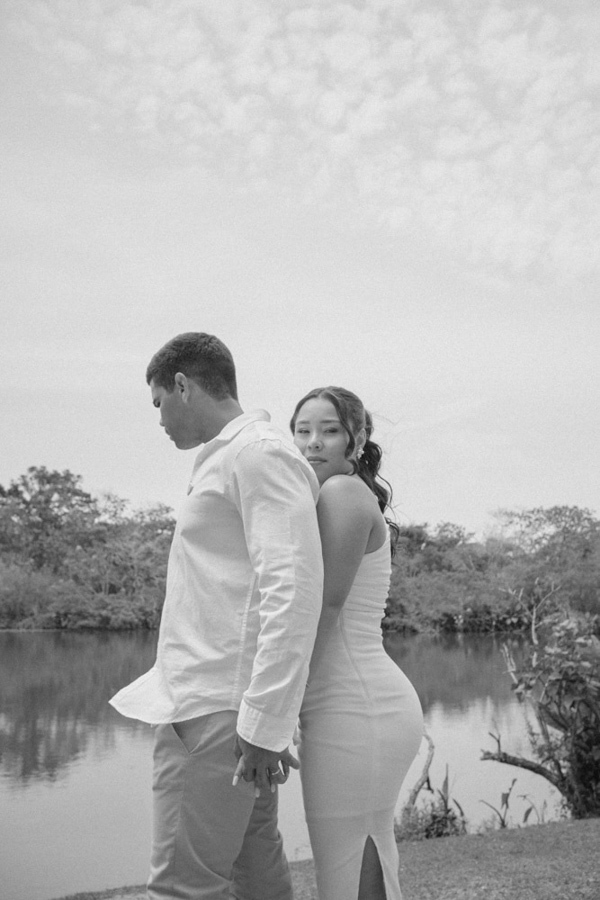 Fotografia de casamento em SJC: Gabrielle e Luiz Carlos posam de costas um para o outro, de mãos dadas, à beira do lago no Parque da Cidade. O registro em preto e branco destaca a silhueta do casal e a serenidade do ensaio em São José dos Campos.