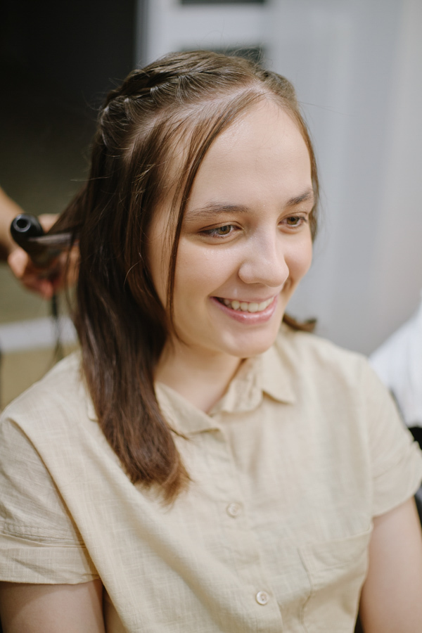 Retrato espontâneo de Anna Clara sorrindo durante a preparação do cabelo. A fotografia documental em Jacareí captura a sensibilidade e a emoção real da debutante, refletindo sua personalidade autêntica em um momento de luz natural e suavidade.