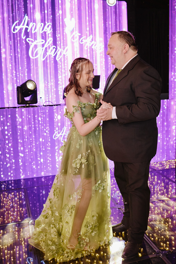 Anna Clara dança com seu pai em um cenário iluminado por painéis de LED roxos. O registro documental captura a emoção real da valsa, unindo o carinho familiar à atmosfera artística e sensível de sua festa de 15 anos em Jacareí.