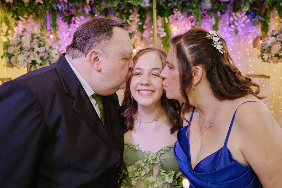 Anna Clara recebe um beijo carinhoso de seus pais em um momento de pura emoção. A fotografia documental em Jacareí eterniza o afeto familiar e a alegria da debutante, destacando sua essência sensível em meio à atmosfera artística da celebração.