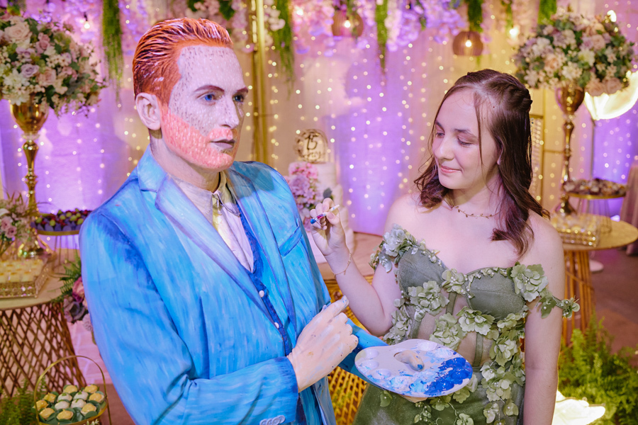 Anna Clara segura uma paleta de tintas ao lado de um artista caracterizado como Van Gogh. O registro documental em Jacareí celebra a paixão da debutante pela arte, transformando sua festa de 15 anos em uma experiência criativa, sensível e única.