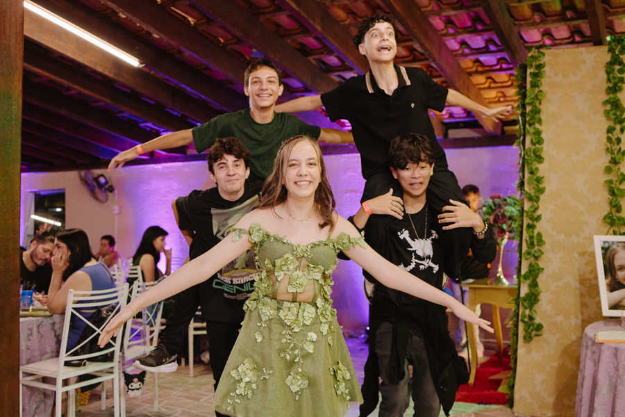 Anna Clara abre os braços sorridente enquanto amigos fazem poses divertidas ao fundo. O registro documental em Jacareí captura a descontração e a alegria real da debutante, celebrando sua personalidade vibrante e o clima de amizade de seus 15 anos.