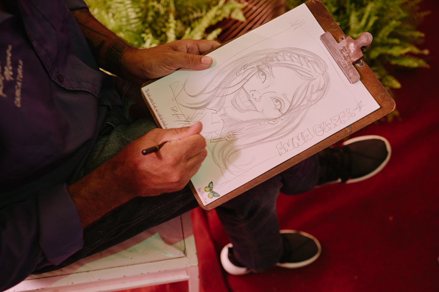Close das mãos de um caricaturista finalizando o desenho de Anna Clara durante sua festa de 15 anos. O registro documental em Jacareí destaca a atmosfera artística e autoral da celebração, onde cada traço reforça a identidade criativa da debutante.