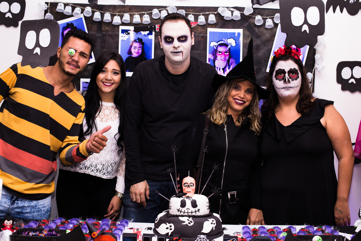 Foto com os pais e convidados de Giullia, posando atrás da mesa do bolo e vestidos a caráter para festa de terror.