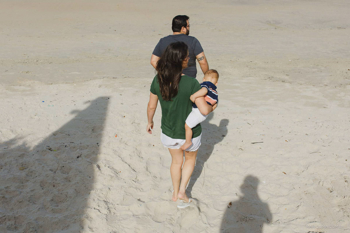 Pais caminhando e segurando o filho no colo na praia do Guarujá