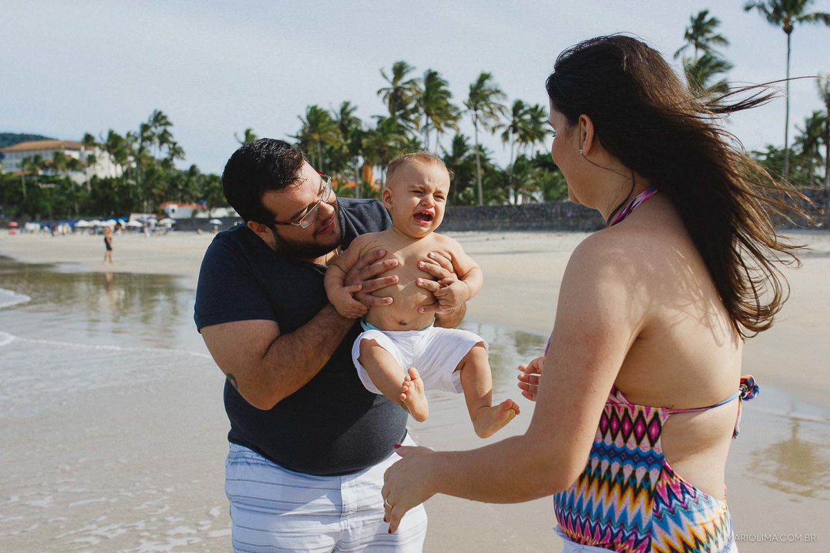 Bebê chorando no colo do pai em praia do Guarujá