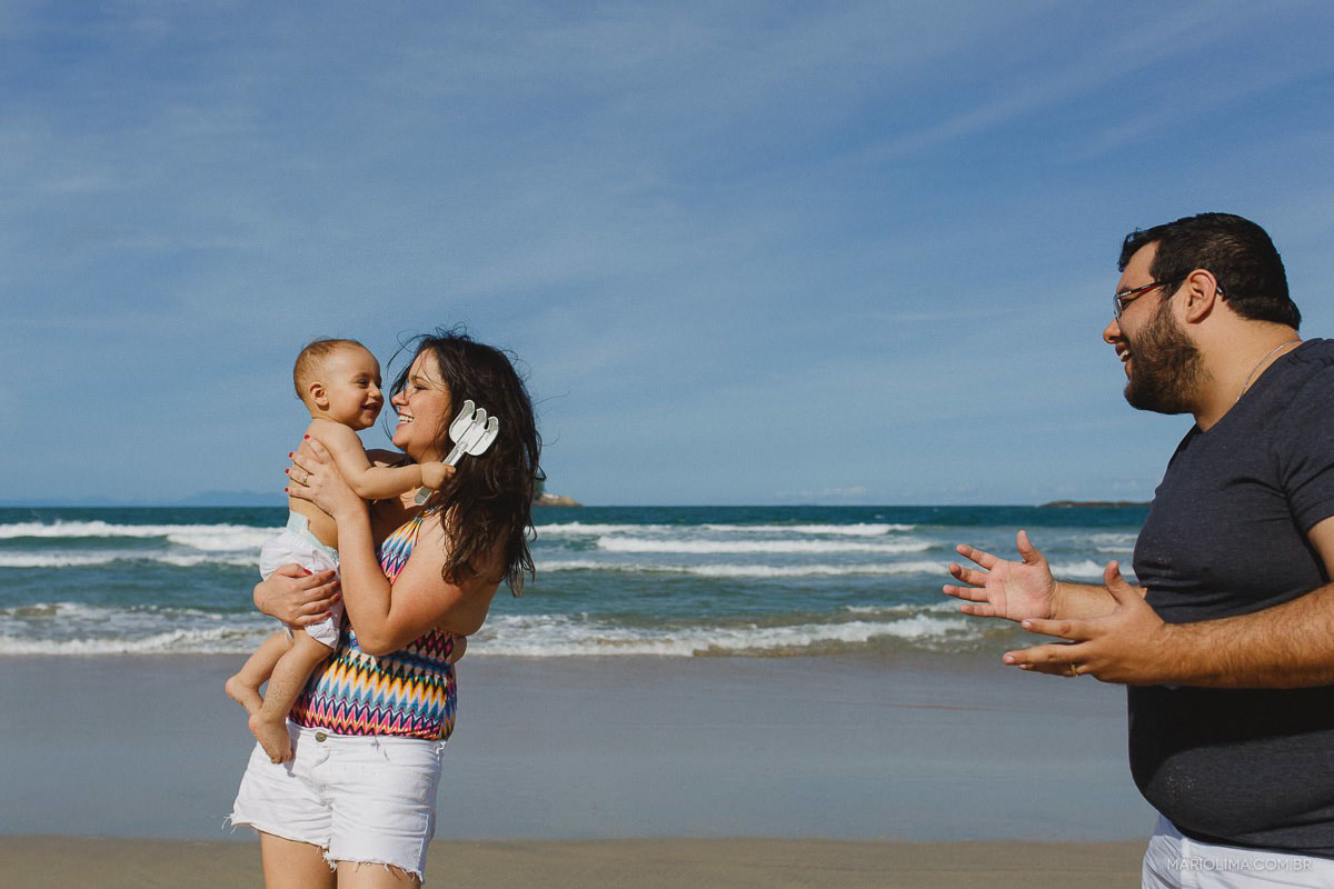 Pai olhando mãe segurar o filho no colo em praia do Guarujá