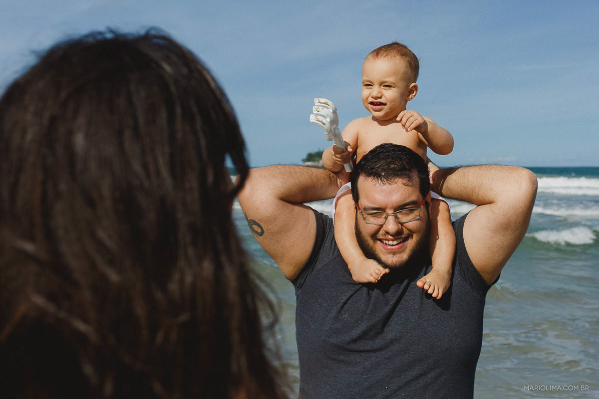 Màe olhando pai com o filho nas costas em praia do Guarujá
