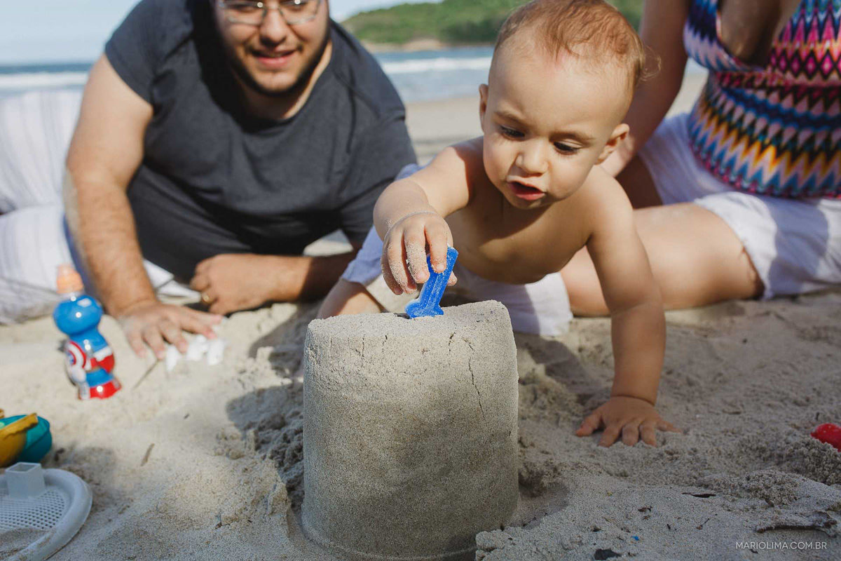 Criança fazendo castelinho de areia com os pais em praia do Guarujá