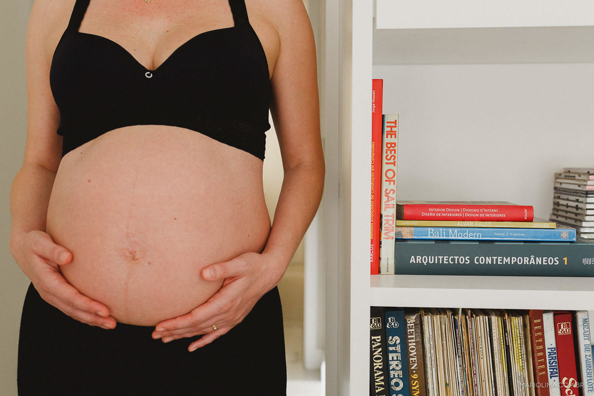 Retrato de barriga de gravida perto da estante da sala